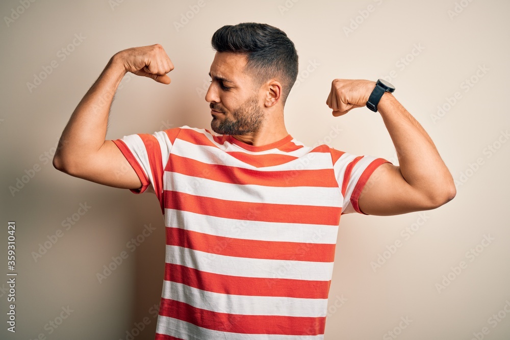 Young handsome man wearing casual striped t-shirt standing over isolated white background showing arms muscles smiling proud. Fitness concept. Young handsome man wearing casual striped t-shirt standing over isolated white background showing arms muscles smiling proud. Fitness concept.