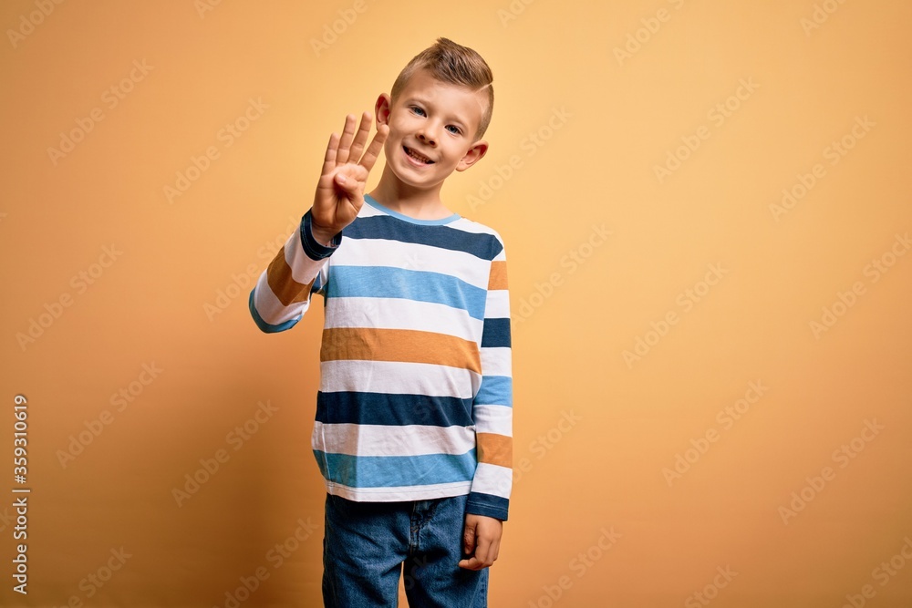 Young little caucasian kid with blue eyes wearing colorful striped shirt over yellow background showing and pointing up with fingers number four while smiling confident and happy. Young little caucasian kid with blue eyes wearing colorful striped shirt over yellow background showing and pointing up with fingers number four while smiling confident and happy.