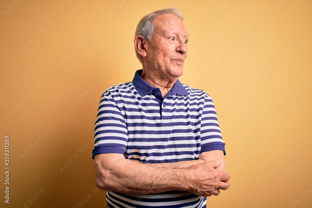Grey haired senior man wearing casual navy striped t-shirt standing over yellow background smiling looking to the side and staring away thinking. Grey haired senior man wearing casual navy striped t-shirt standing over yellow background smiling looking to the side and staring away thinking.