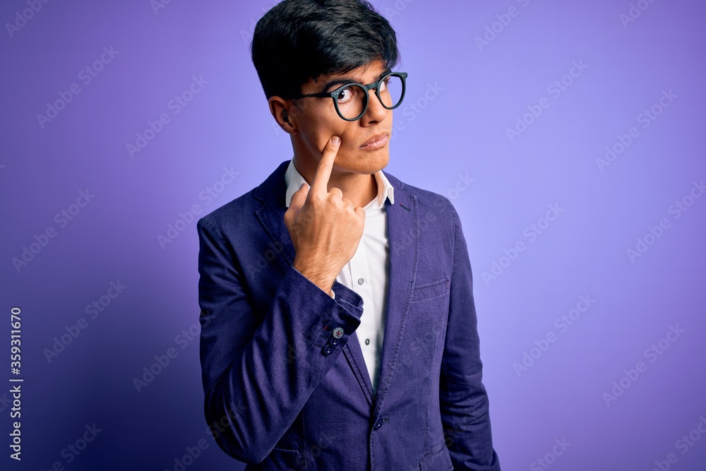 Young handsome business man wearing jacket and glasses over isolated purple background Pointing to the eye watching you gesture, suspicious expression Young handsome business man wearing jacket and glasses over isolated purple background Pointing to the eye watching you gesture, suspicious expression