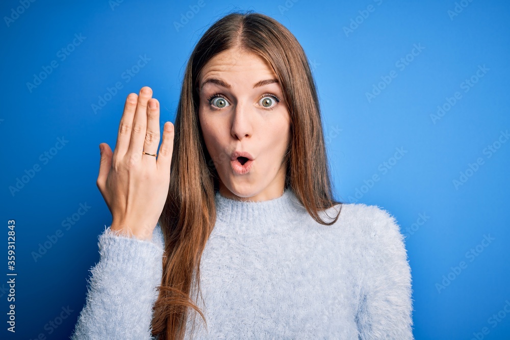 Young beautiful redhead woman wearing wedding ring on finger over blue background scared in shock with a surprise face, afraid and excited with fear expression Young beautiful redhead woman wearing wedding ring on finger over blue background scared in shock with a surprise face, afraid and excited with fear expression