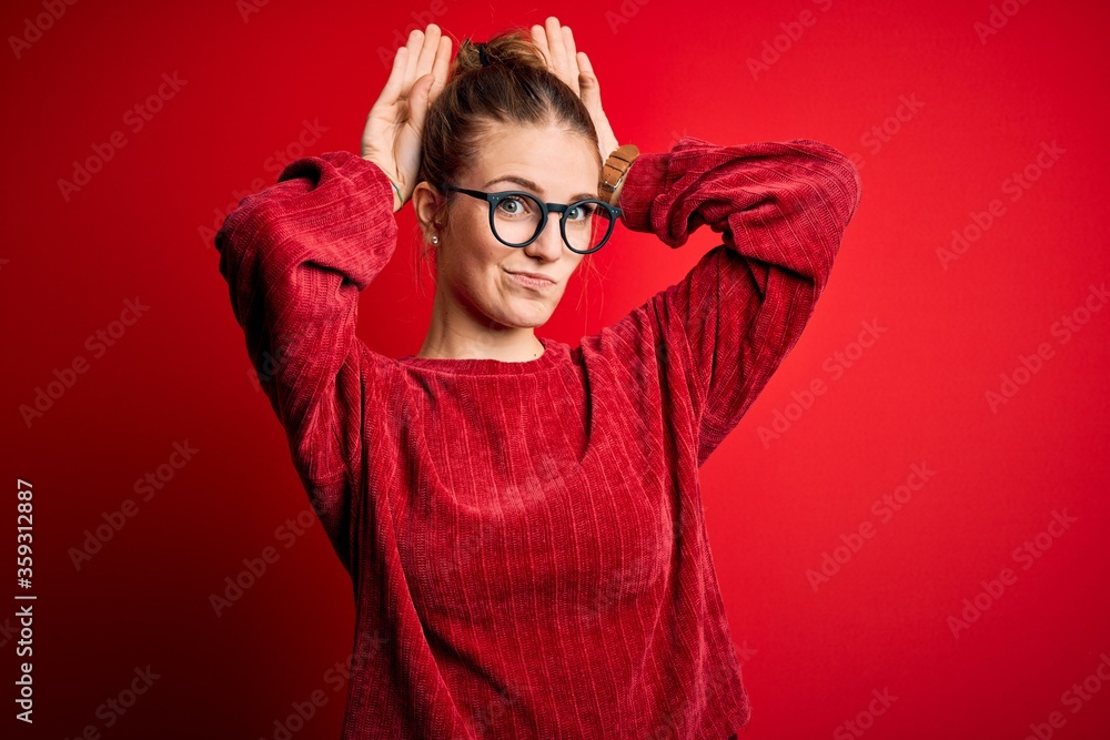 Young beautiful redhead woman wearing casual sweater over isolated red background Doing bunny ears gesture with hands palms looking cynical and skeptical. Easter rabbit concept. Young beautiful redhead woman wearing casual sweater over isolated red background Doing bunny ears gesture with hands palms looking cynical and skeptical. Easter rabbit concept.