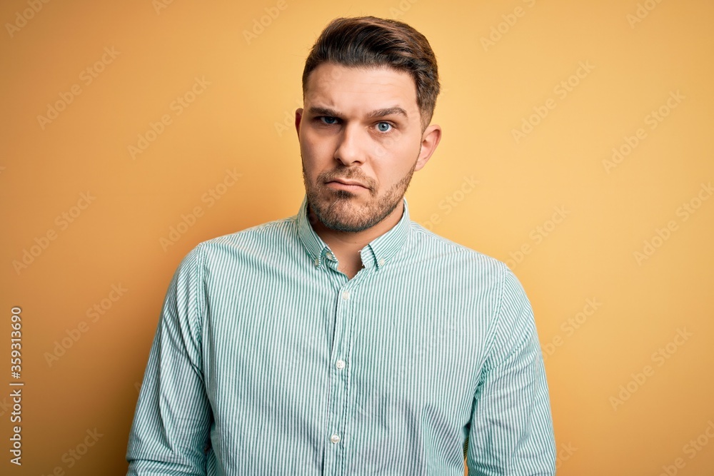 Young business man with blue eyes wearing elegant green shirt over yellow background skeptic and nervous, frowning upset because of problem. Negative person. Young business man with blue eyes wearing elegant green shirt over yellow background skeptic and nervous, frowning upset because of problem. Negative person.