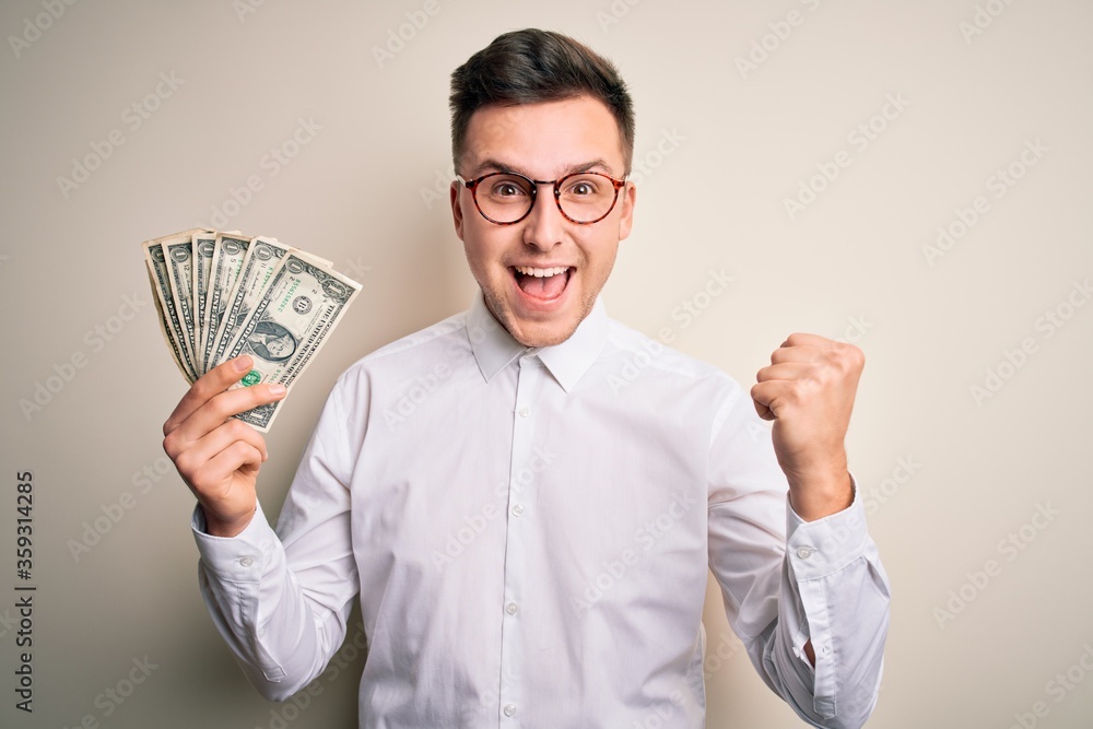 Young handsome caucasian business man holding bunch of one dollar banknotes screaming proud and celebrating victory and success very excited, cheering emotion Young handsome caucasian business man holding bunch of one dollar banknotes screaming proud and celebrating victory and success very excited, cheering emotion
