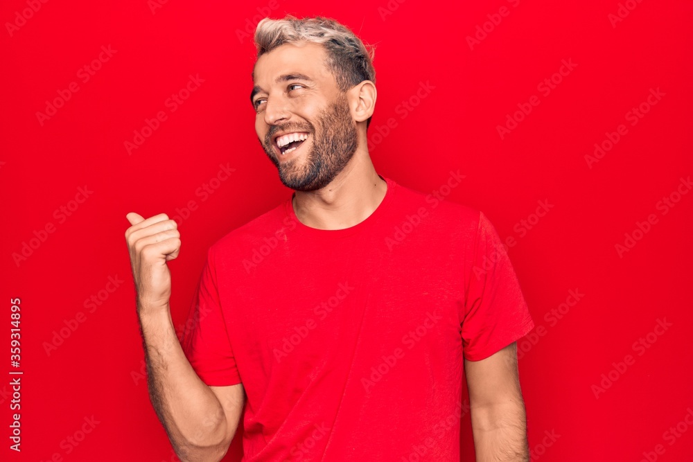 Young handsome blond man wearing casual red t-shirt standing over isolated red background pointing thumb up to the side smiling happy with open mouth Young handsome blond man wearing casual red t-shirt standing over isolated red background pointing thumb up to the side smiling happy with open mouth