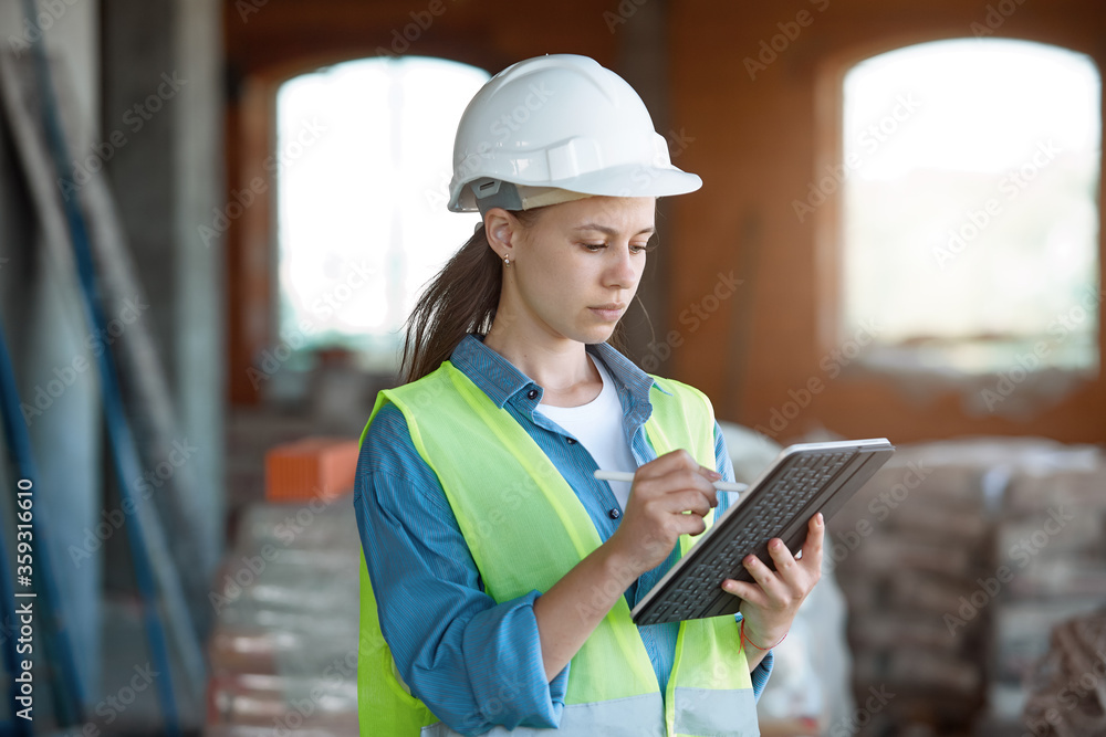 Absorbed in the work of a woman engineer working with a tablet on the background of the construction site. Portrait of a young architect, protective equipment. Selective focus. Absorbed in the work of a woman engineer working with a tablet on the background of the construction site. Portrait of a young architect, protective equipment. Selective focus.