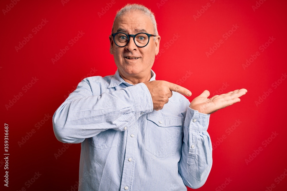 Middle age handsome hoary man wearing casual striped shirt and glasses over red background amazed and smiling to the camera while presenting with hand and pointing with finger. Middle age handsome hoary man wearing casual striped shirt and glasses over red background amazed and smiling to the camera while presenting with hand and pointing with finger.