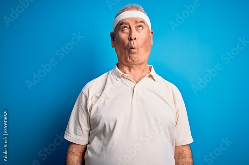 Middle age hoary sportsman doing sport wearing sportswear over isolated blue background making fish face with lips, crazy and comical gesture. Funny expression. © Krakenimages.com