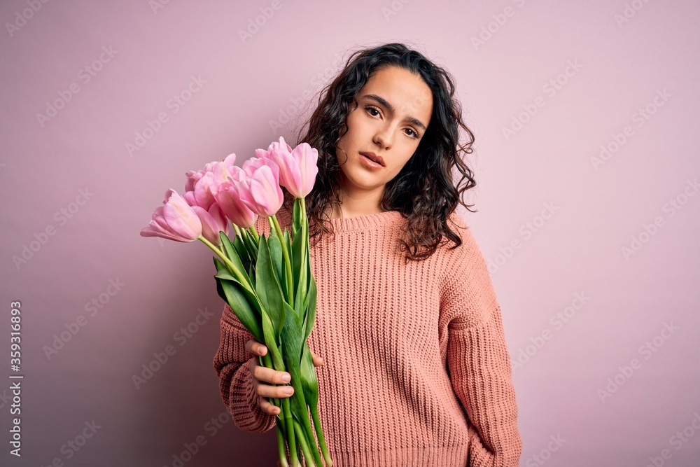 Young beautiful romantic woman with curly hair holding bouquet of pink tulips looking sleepy and tired, exhausted for fatigue and hangover, lazy eyes in the morning. Young beautiful romantic woman with curly hair holding bouquet of pink tulips looking sleepy and tired, exhausted for fatigue and hangover, lazy eyes in the morning.