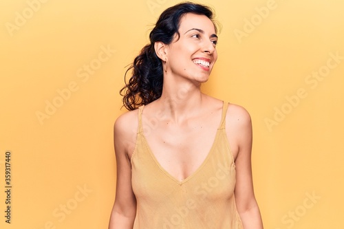Young beautiful hispanic woman wearing casual clothes looking away to side with smile on face, natural expression. laughing confident.
