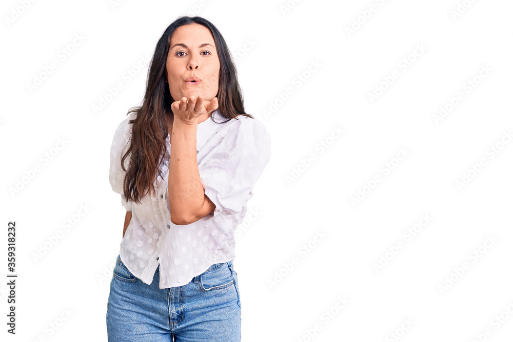 Young beautiful brunette woman wearing casual shirt looking at the camera blowing a kiss with hand on air being lovely and sexy. love expression. Young beautiful brunette woman wearing casual shirt looking at the camera blowing a kiss with hand on air being lovely and sexy. love expression.