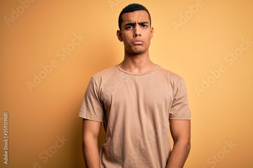 Young handsome african american man wearing casual t-shirt standing over yellow background depressed and worry for distress, crying angry and afraid. Sad expression.