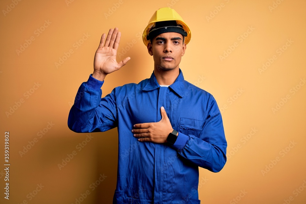 Young handsome african american worker man wearing blue uniform and security helmet Swearing with hand on chest and open palm, making a loyalty promise oath