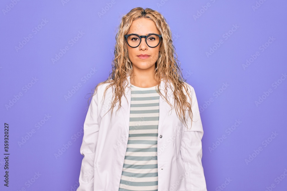 Young beautiful blonde scientist woman wearing coat and glasses over purple background with serious expression on face. Simple and natural looking at the camera. Young beautiful blonde scientist woman wearing coat and glasses over purple background with serious expression on face. Simple and natural looking at the camera.