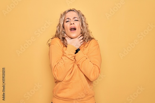 Young beautiful blonde sporty woman wearing casual sweatshirt over yellow background shouting suffocate because painful strangle. Health problem. Asphyxiate and suicide concept.