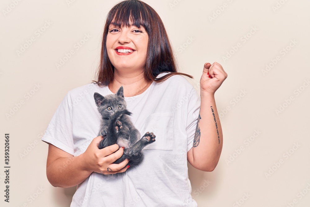 Young plus size woman holding cat screaming proud, celebrating victory and success very excited with raised arm Young plus size woman holding cat screaming proud, celebrating victory and success very excited with raised arm