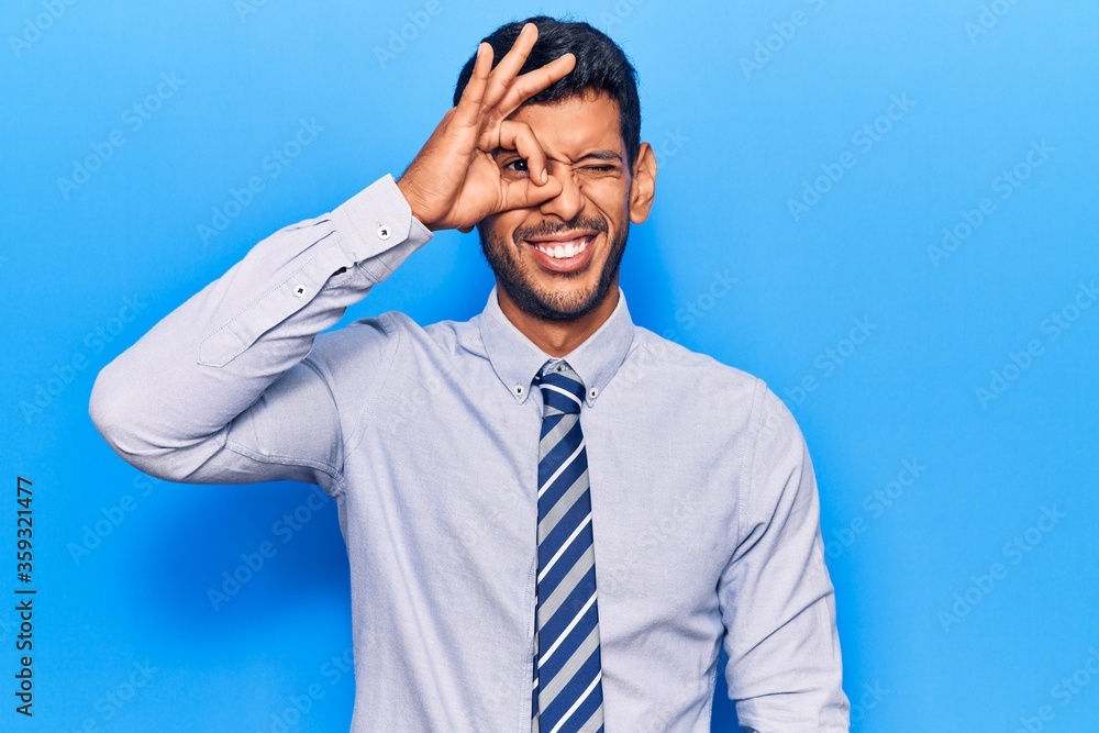 Young latin man wearing business clothes smiling happy doing ok sign with hand on eye looking through fingers Young latin man wearing business clothes smiling happy doing ok sign with hand on eye looking through fingers