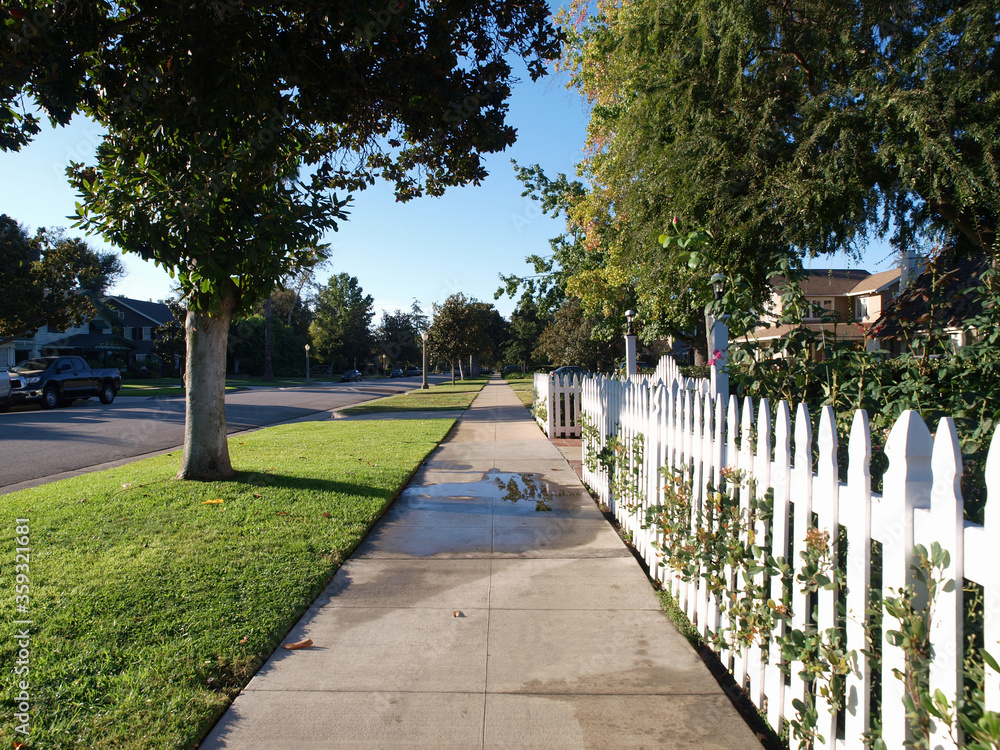 Pretty picket fence and sidewalk on a typical suburban residential street.