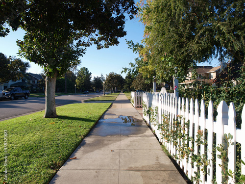 Pretty picket fence and sidewalk on a typical suburban residential street.