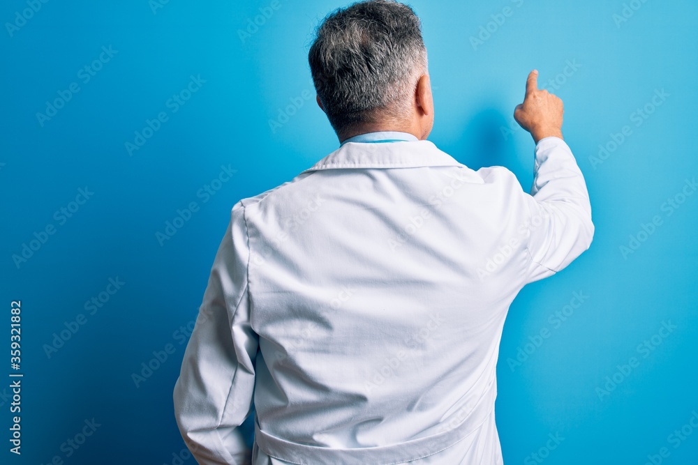 Middle age handsome grey-haired doctor man wearing coat and blue stethoscope Posing backwards pointing ahead with finger hand Middle age handsome grey-haired doctor man wearing coat and blue stethoscope Posing backwards pointing ahead with finger hand