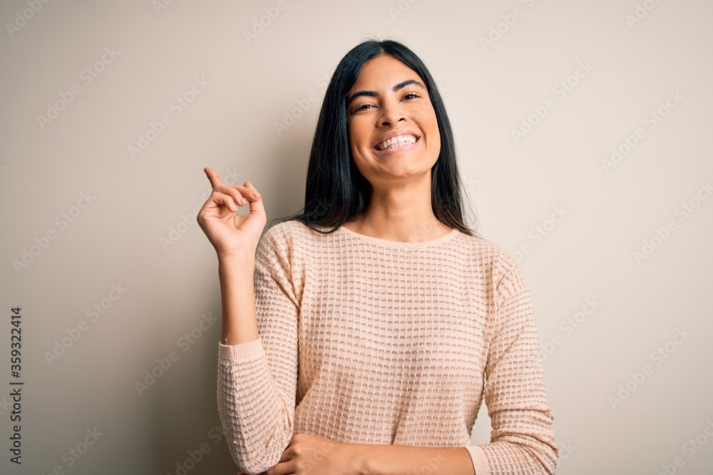 Young beautiful hispanic woman wearing elegant pink sweater over isolated background with a big smile on face, pointing with hand and finger to the side looking at the camera. Young beautiful hispanic woman wearing elegant pink sweater over isolated background with a big smile on face, pointing with hand and finger to the side looking at the camera.