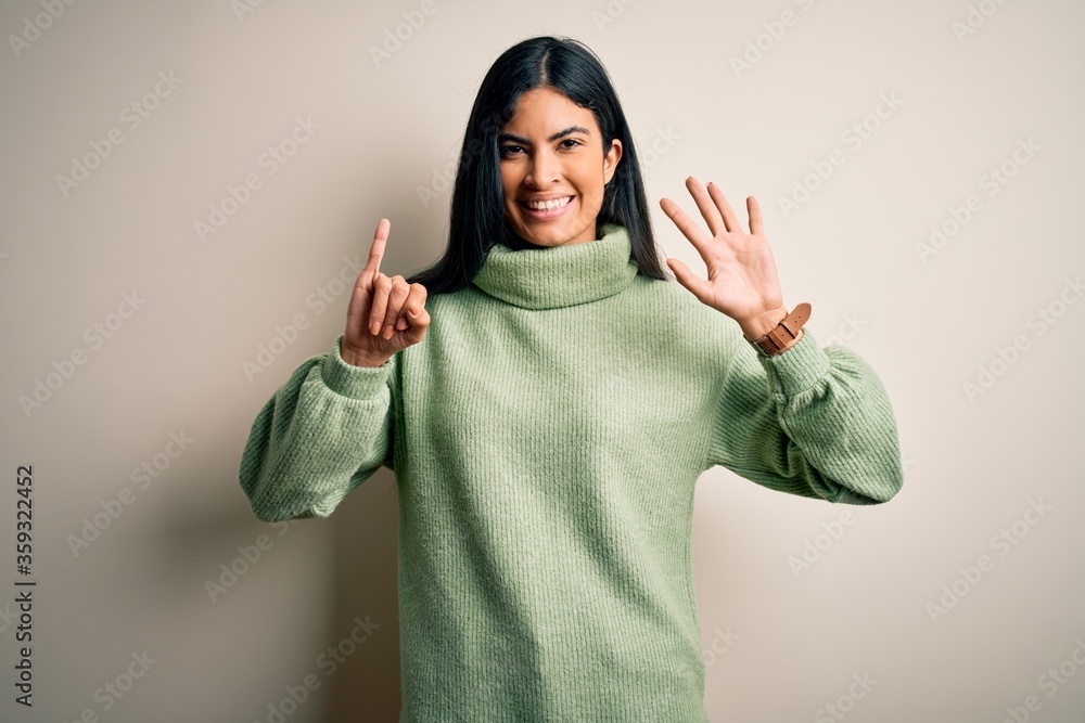 Young beautiful hispanic woman wearing green winter sweater over isolated background showing and pointing up with fingers number six while smiling confident and happy. Young beautiful hispanic woman wearing green winter sweater over isolated background showing and pointing up with fingers number six while smiling confident and happy.