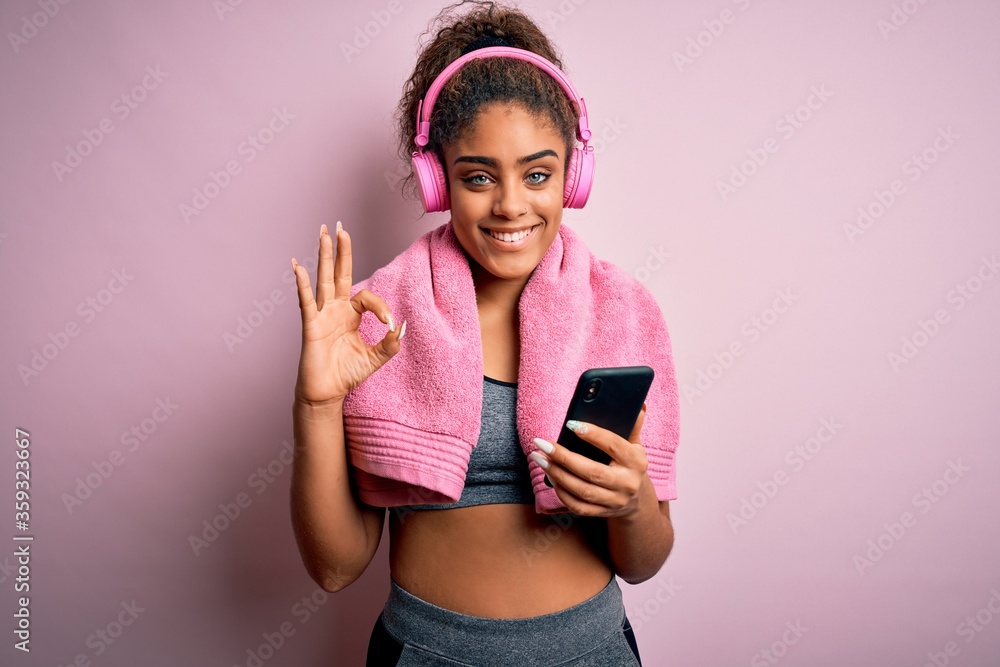 Young african american sportswoman playing tennis using racket over isolated pink background doing ok sign with fingers, excellent symbol