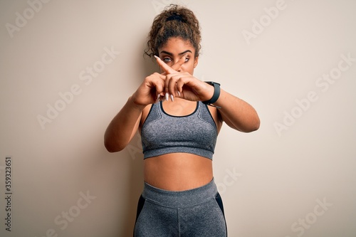 Young african american sportswoman doing sport wearing sportswear over white background Rejection expression crossing fingers doing negative sign