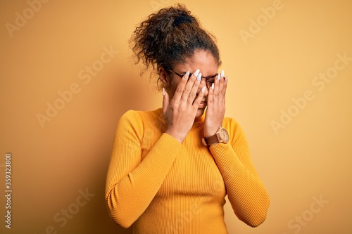 Young beautiful african american girl wearing sweater and glasses over yellow background rubbing eyes for fatigue and headache, sleepy and tired expression. Vision problem