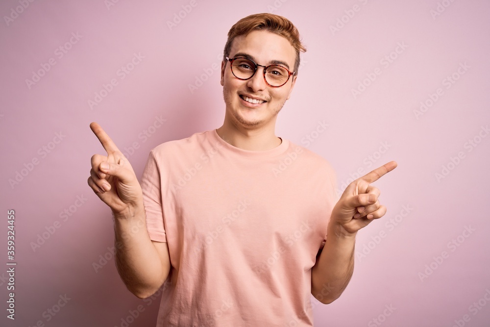 Young handsome redhead man wearing casual t-shirt standing over isolated pink background smiling confident pointing with fingers to different directions. Copy space for advertisement