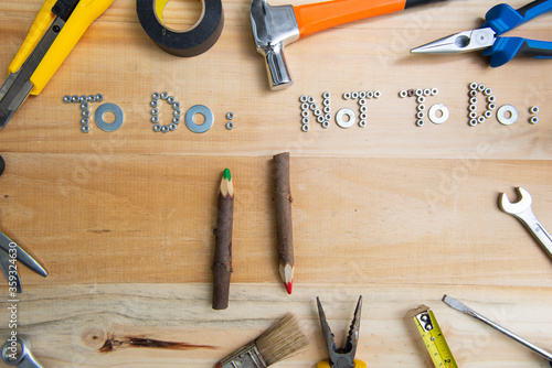 Top view of the phrases "to do" and "not to do" made of nuts and washers on a wooden surface for planning the work. Construction tools framing wooden background shot from above.