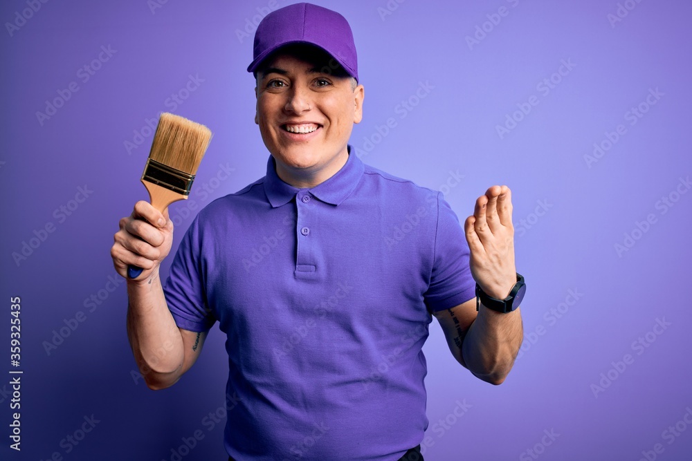 Young modern decorator painter man holding paint brush over purple background very happy and excited, winner expression celebrating victory screaming with big smile and raised hands