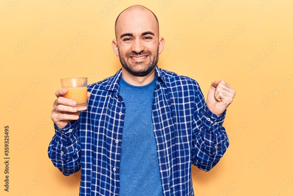 Young handsome bald man drinking glass of healthy orange juice screaming  proud, celebrating victory and success very excited with raised arm Stock  Photo | Adobe Stock