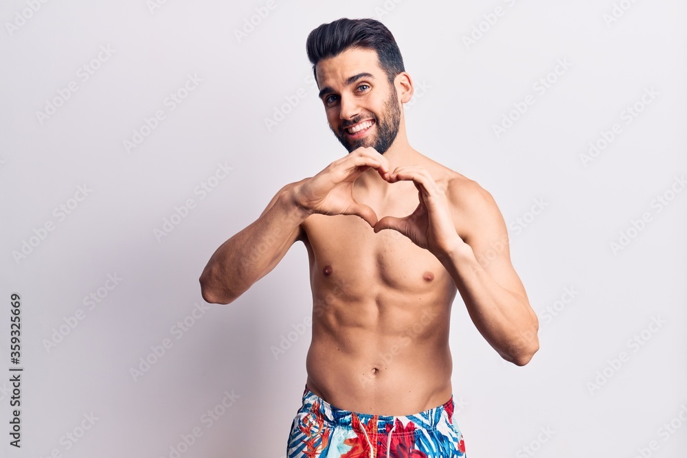 Young handsome man with beard shirtless wearing swimwear smiling in love doing heart symbol shape with hands. romantic concept. Young handsome man with beard shirtless wearing swimwear smiling in love doing heart symbol shape with hands. romantic concept.