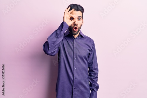 Young handsome man with beard wearing casual shirt doing ok gesture shocked with surprised face, eye looking through fingers. unbelieving expression. © Krakenimages.com