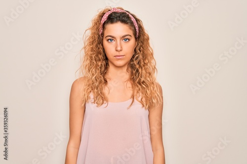 Young beautiful woman with blue eyes wearing casual t-shirt and diadem over pink background with serious expression on face. Simple and natural looking at the camera.