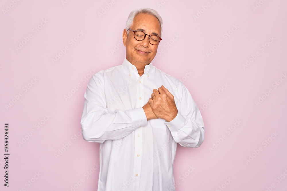 Middle age senior grey-haired man wearing glasses and business shirt over pink background smiling with hands on chest with closed eyes and grateful gesture on face. Health concept. Middle age senior grey-haired man wearing glasses and business shirt over pink background smiling with hands on chest with closed eyes and grateful gesture on face. Health concept.