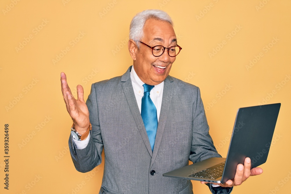Middle age senior grey-haired business man wearing glasses working using computer laptop very happy and excited, winner expression celebrating victory screaming with big smile and raised hands Middle age senior grey-haired business man wearing glasses working using computer laptop very happy and excited, winner expression celebrating victory screaming with big smile and raised hands