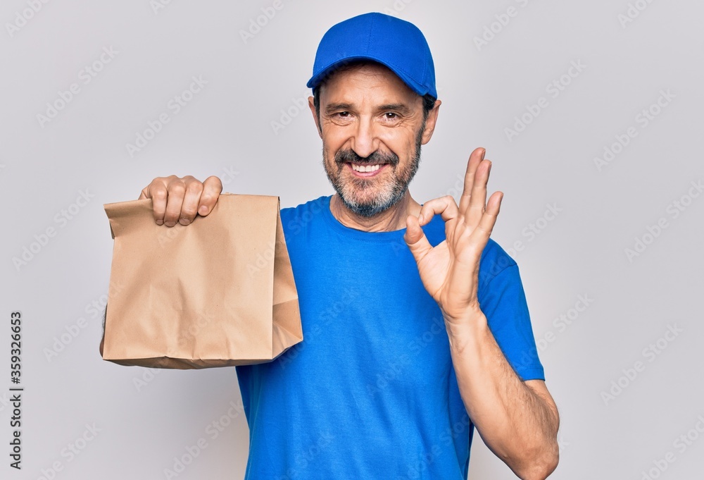 Middle age handsome delivery man wearing cap holding paper bag with takeaway food doing ok sign with fingers, smiling friendly gesturing excellent symbol Middle age handsome delivery man wearing cap holding paper bag with takeaway food doing ok sign with fingers, smiling friendly gesturing excellent symbol