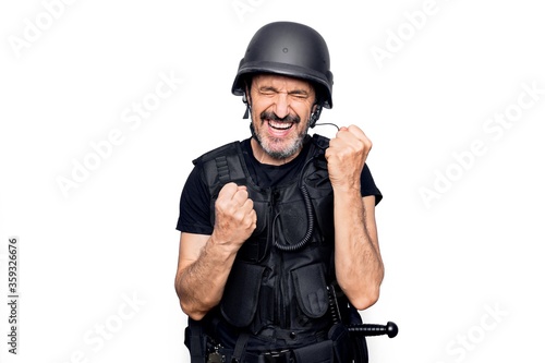 Middle age handsome policeman wearing police bulletproof vest and security helmet celebrating surprised and amazed for success with arms raised and eyes closed