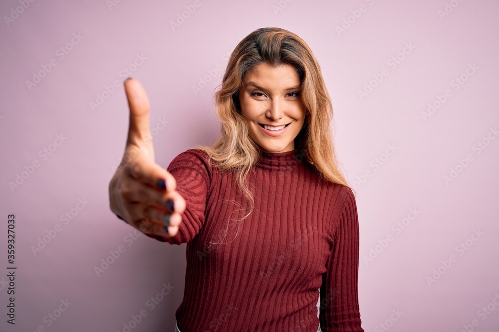 Young beautiful blonde woman wearing casual sweater over isolated pink background smiling friendly offering handshake as greeting and welcoming. Successful business. Young beautiful blonde woman wearing casual sweater over isolated pink background smiling friendly offering handshake as greeting and welcoming. Successful business.