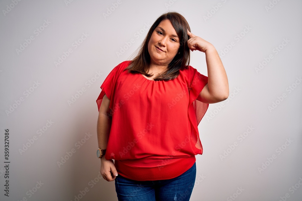Beautiful brunette plus size woman wearing casual red t-shirt over isolated white background Smiling pointing to head with one finger, great idea or thought, good memory Beautiful brunette plus size woman wearing casual red t-shirt over isolated white background Smiling pointing to head with one finger, great idea or thought, good memory