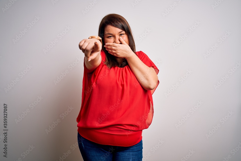 Beautiful brunette plus size woman wearing casual red t-shirt over isolated white background laughing at you, pointing finger to the camera with hand over mouth, shame expression Beautiful brunette plus size woman wearing casual red t-shirt over isolated white background laughing at you, pointing finger to the camera with hand over mouth, shame expression