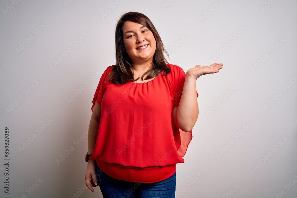 Beautiful brunette plus size woman wearing casual red t-shirt over isolated white background smiling cheerful presenting and pointing with palm of hand looking at the camera. Beautiful brunette plus size woman wearing casual red t-shirt over isolated white background smiling cheerful presenting and pointing with palm of hand looking at the camera.