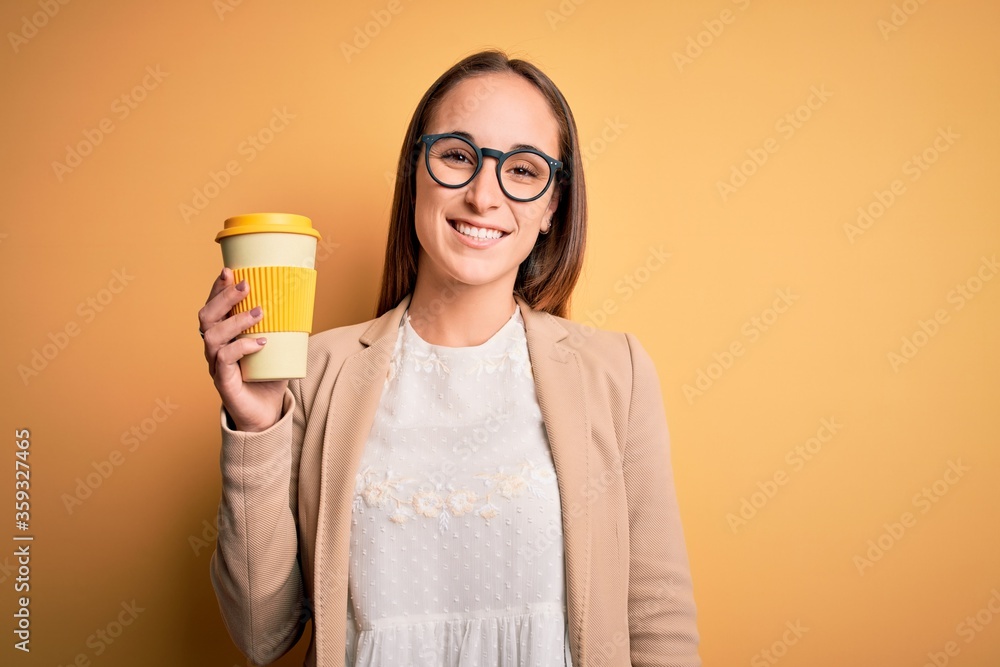 Young beautiful businesswoman drinking cup of takeaway coffee over yellow background with a happy face standing and smiling with a confident smile showing teeth Young beautiful businesswoman drinking cup of takeaway coffee over yellow background with a happy face standing and smiling with a confident smile showing teeth