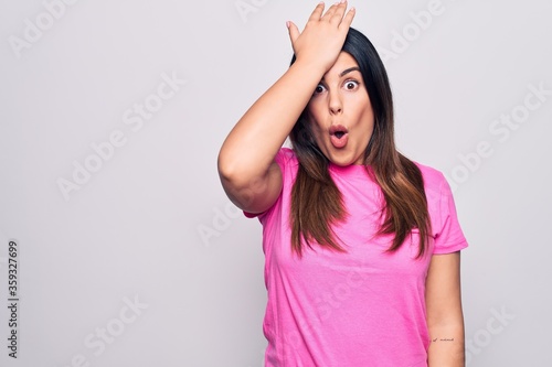 Young beautiful brunette woman wearing casual pink t-shirt standing over white background surprised with hand on head for mistake  remember error. Forgot  bad memory concept.