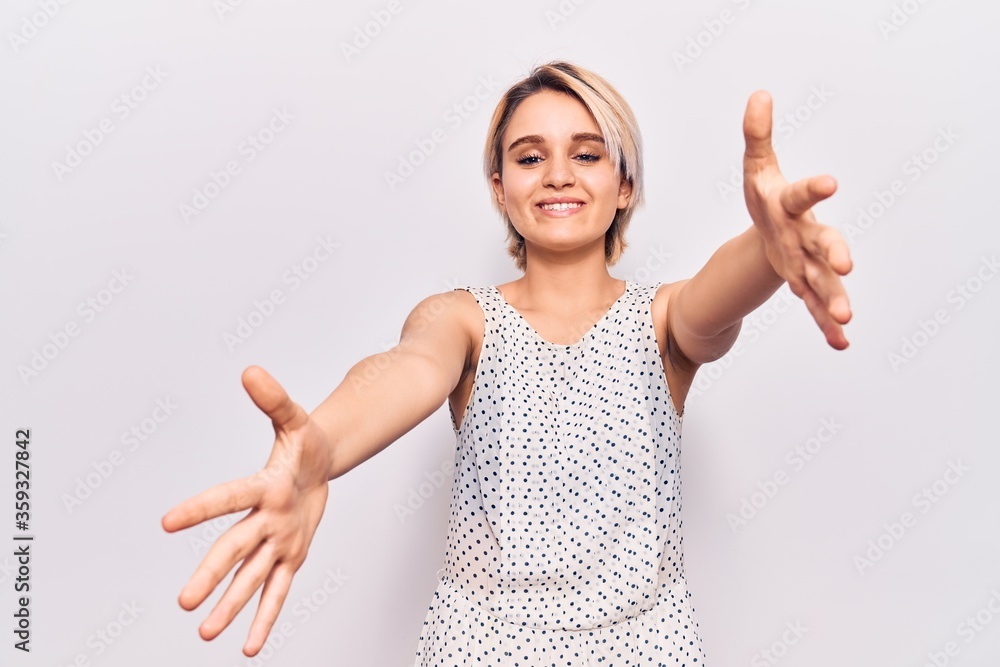 Young beautiful blonde woman wearing casual clothes looking at the camera smiling with open arms for hug. cheerful expression embracing happiness. Young beautiful blonde woman wearing casual clothes looking at the camera smiling with open arms for hug. cheerful expression embracing happiness.