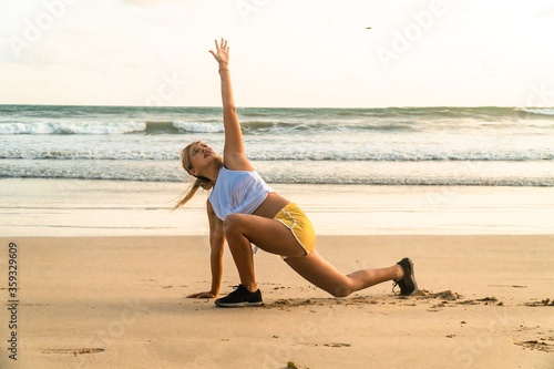 Young woman doing yoga stretching on the beach. Outdoor workout by the sea. Staying healthy and active during pandemic