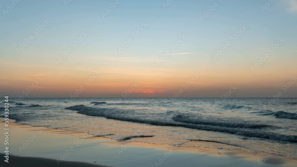 Time lapse: Beach sunset video with reflection on wet sand and incoming ocean waves. A beached foreground log adds interest. Seamless loop. Clip contain noise and blurry. Shot at 2160p. 4K. Time lapse: Beach sunset video with reflection on wet sand and incoming ocean waves. A beached foreground log adds interest. Seamless loop. Clip contain noise and blurry. Shot at 2160p. 4K.