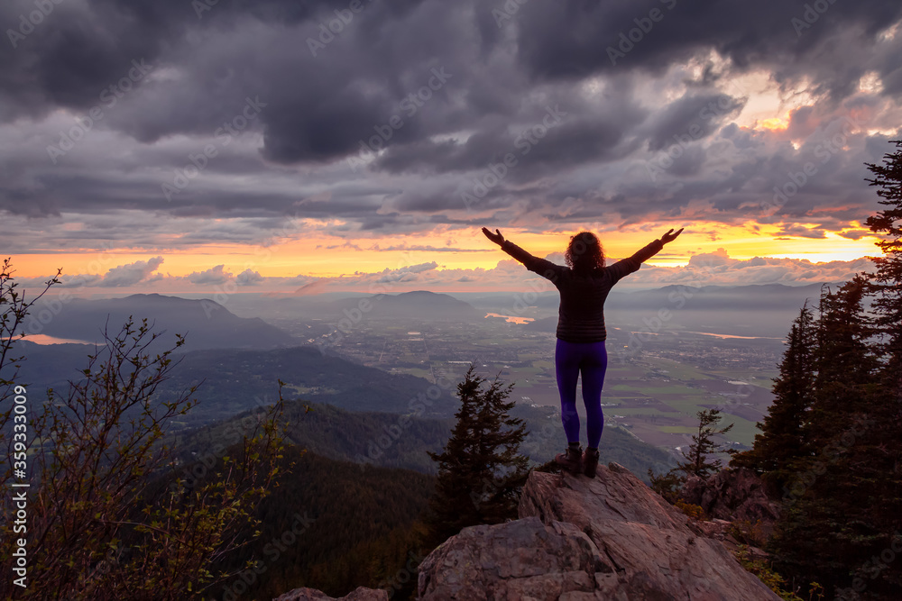 Adventurous Girl on top of a Rocky Mountain overlooking the beautiful Canadian Nature Landscape during a dramatic Sunset. Taken in Chilliwack, East of Vancouver, British Columbia, Canada.